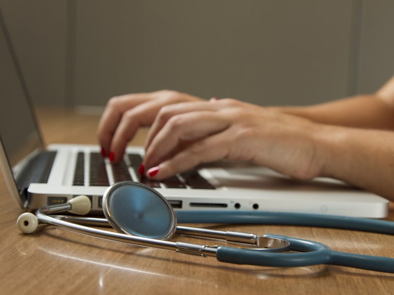 A clinician working at a laptop with a stethoscope nearby — technology and medicine together